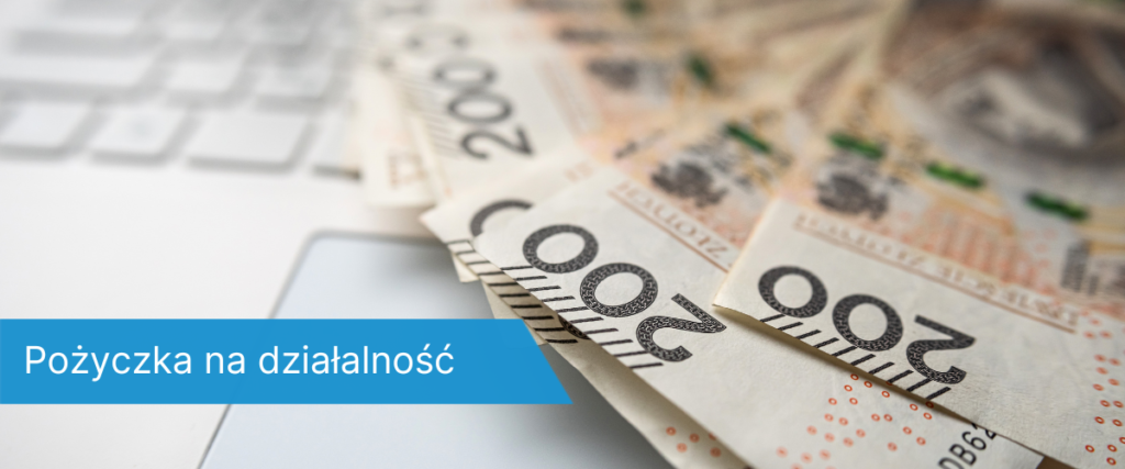 Rozłożone banknoty 200 zł leżące na białej klawiaturze laptopa;